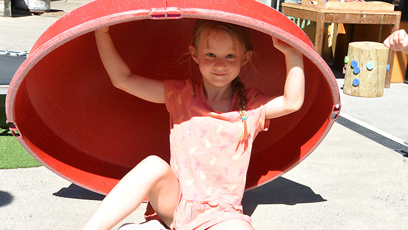 girl playing under big container at daycare
