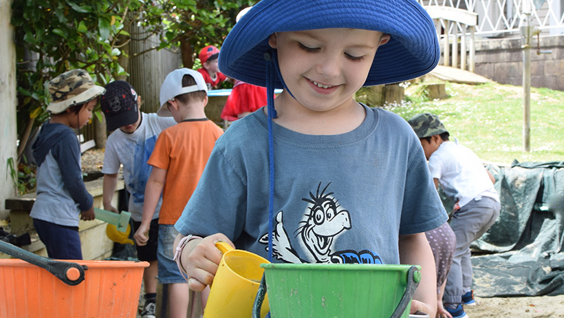 boy in hat with bucket and cup at childcare