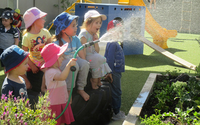 children watering plants with hose at daycare