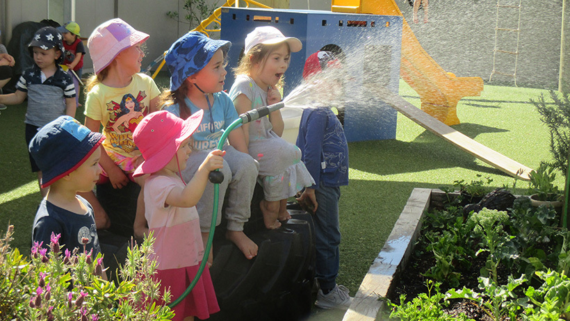 children watering plants with hose at daycare